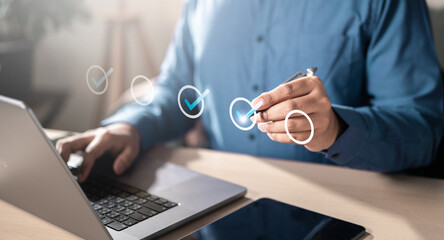 check, checkmark, management, marketing, program, strategy, touch, information, social, analysis. A man is using a laptop, He is holding a pen and is looking at a screen with a check mark on it. © Garun Studios
