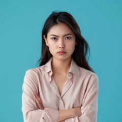 Displeased young Asian woman with dark hair expresses disagreement while posing against a blue backdrop, showcasing her fashion sense in neat attire