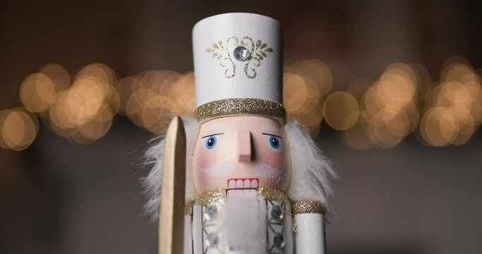 Nutcracker in a white costume, holding a sword, illuminated by golden bokeh lights, adding a festive touch of elegance to any Christmas setting