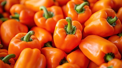 A close-up shot of a pile of bright orange bell peppers with green stems.