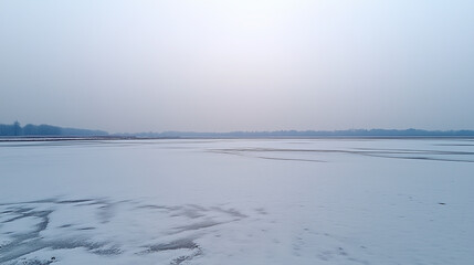 Obraz premium A frozen lake with a hazy sky and a tree line in the distance.