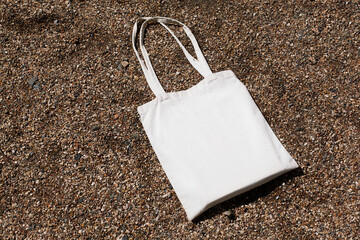 White cotton or mesh bag on beach sand background. Zero waste, no plastic, eco friendly shopping,...