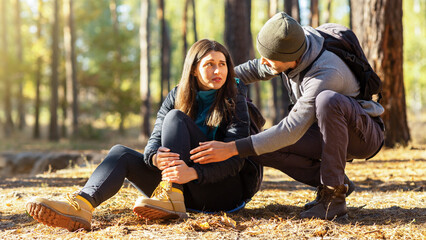 Young guy rubbing his upset girlfriend injured leg, hiking together at forest, copy space