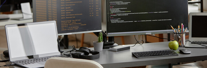 Website header shot of programmer desk setup with laptop and multiple computer screens displaying...