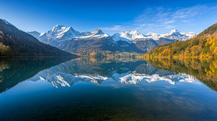Naklejka premium Picturesque view of a mountain lake with snow-capped peaks reflected in the still water.
