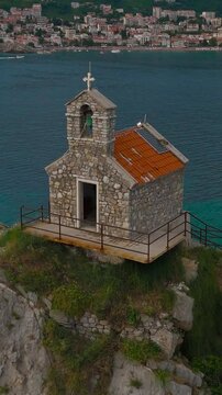 The church on an island-rock rising from the sea is a magical sight, harmoniously integrated into the natural landscape. Petrovac, Montenegro. 4k drone video. Vertical video for reels.