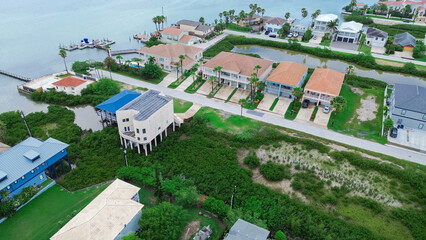 Beach houses on stilts for flood management and upscale villa mansion houses with private wooden jetty boat ramp pier, Laguna Bay South Padre Island, residential area and vacation rental, aerial
