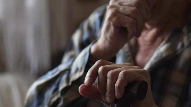an elderly person 70-79 years old coughs while sitting holding a walking stick, a pensioner coughs heavily into his fist while inside