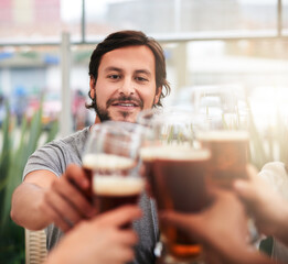 Beer, cheers and man with friends at cafe for lunch, social celebration or relax with alcohol at table together. Happy, group and people toast in restaurant with drink, solidarity and weekend reunion