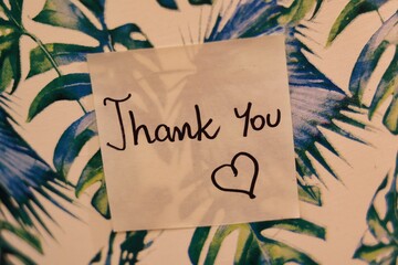 A sticky note with the inscription "thank you" on a floral pattern background © Gosia
