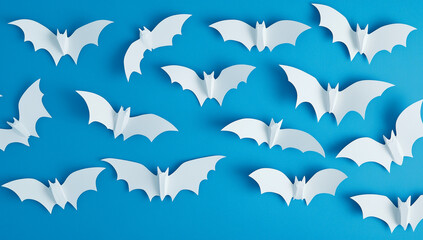 Naklejka premium A pattern of white bats on a blue background creates a spooky Halloween decoration in a flat lay, featuring black paper cut bat silhouettes from a top view.