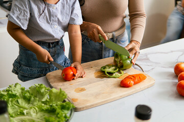 Mother and little daughter preparing a meal in the kitchen. The image highlights family bonding, healthy eating.