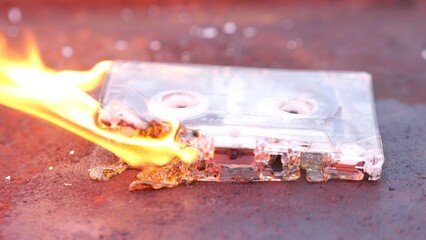 Audio cassette melting in flames on rusty background