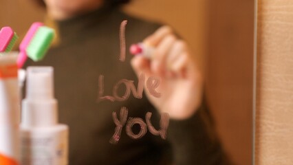 Woman writing i love you on bathroom mirror