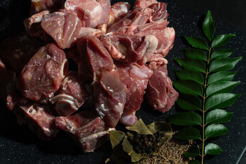 Freshly cut goat meat pieces with herbs and spices like bay leaves, cumin seeds, and peppercorns. Perfect for food preparation, recipes, and culinary projects.