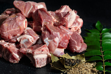 Freshly cut goat meat pieces with herbs and spices like bay leaves, cumin seeds, and peppercorns. Perfect for food preparation, recipes, and culinary projects.