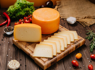 Delicious cheese wheel and slice on a wooden board with fresh herbs, garlic, and cherry tomatoes