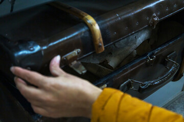 A person wearing a bright yellow sweater is holding a brown suitcase