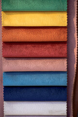 A vertical arrangement of fabric swatches in vibrant colors and textured surfaces, offering a variety of materials for design and upholstery.
