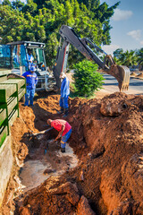 african american construction workers with an excavator fixing a blocked damaged broken drainage...