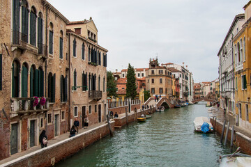 Venetian Canal Scene with Historic Architecture and Bridge. A vibrant canal in Venice with historic buildings, a pedestrian bridge, and boats, under a colorful sky.