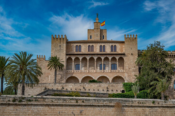 Fototapeta premium The Royal Palace of La Almudaina in Palma de mallorca with trees in front during great weather, view from the distance, Majorca
