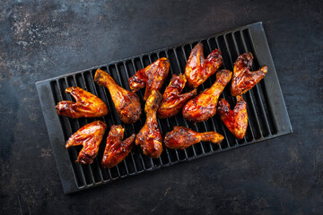 Authentical barbecue chicken wings and drumsticks with hot chili sauce as marinade served as top view on a rustic grill grate