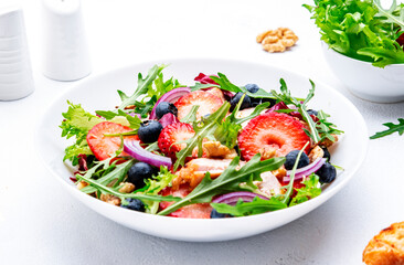 Foodie food salad with strawberry, grilled chicken, arugula, blueberries and walnuts with ciabatta, white table., top view