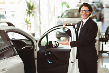 Vip Service. Smiling Male Dealer In Specs Showing New Automobile, Opening Door Inviting Customers, Copy Space