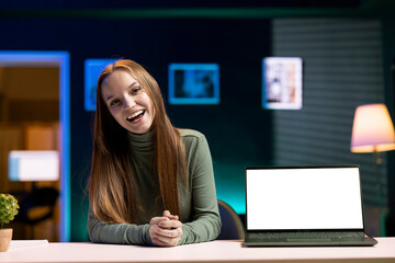 Cheerful girl does influencer marketing by presenting followers mockup laptop sponsored by company. Happy content creator fulfilling brand advertising contract by showcasing isolated screen notebook