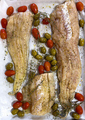 Preparing to bake fish fillets in the oven with cherry tomatoes and green olives