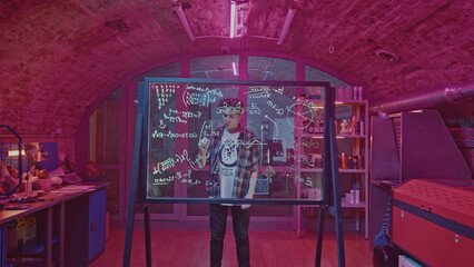 Young man solves equations in laboratory. Media. Student solves mathematical equations in secret classroom. Laboratory for experiments with mathematical calculations on blackboard