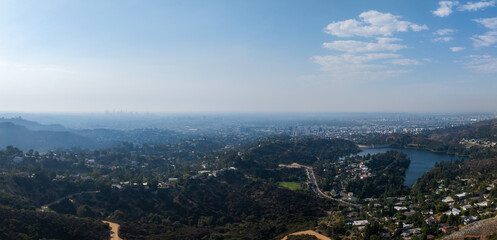 An expansive aerial view of Los Angeles features a reservoir surrounded by greenery and residential areas, with the city skyline in the distance.