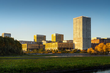 Modern apartment building against the sky, grass field and park in the foreground.