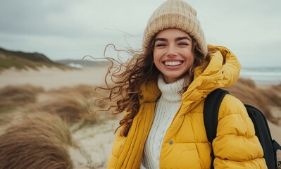 Smiling woman in oversized yellow puffer jacket and knit beanie standing on a windy beach