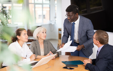 Positive partner men and women discussing a problem sitting around table in meeting room