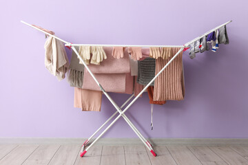Dryer with winter clothes on floor near purple wall