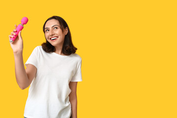Beautiful young woman with vibrator on yellow background