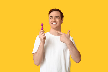 Handsome young man pointing at anal plug on yellow background
