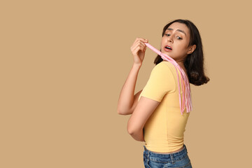 Emotional young woman with whip on beige background