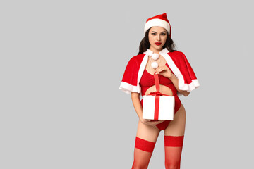 Beautiful young sexy woman in lingerie and Santa hat with gift box on grey background