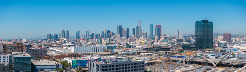 Fototapeta premium Panoramic aerial view of downtown Los Angeles with skyscrapers, including U.S. Bank Tower, and the Sixth Street Viaduct under a clear blue sky.