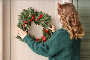 Woman in green sweater hanging Christmas mistletoe wreath on door © Pixel-Shot