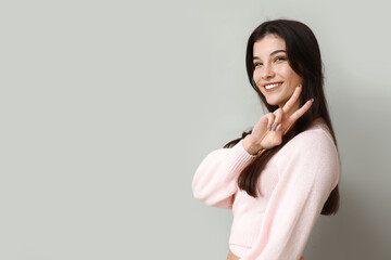 Obraz premium Young woman showing peace sign on light background