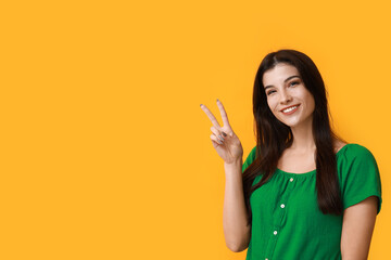 Young woman showing peace sign on yellow background
