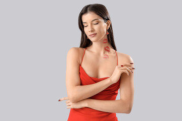 Attractive young woman with lipstick kiss marks on her neck against light background
