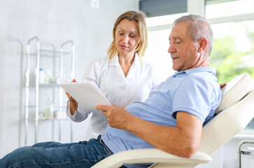 Obraz premium Adult female medic gives contract to sign to elderly man patient in medical room