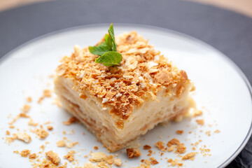 Delicious napoleon cake with flaky crust, creamy custard, and mint leaves on white plate. Perfect sweet treat with buttery, crunchy texture. Ideal for cafes and restaurants