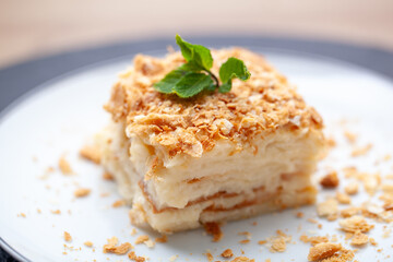 Decadent napoleon cake with mint on white plate, crumbs scattered, promises burst of sweetness. Perfect treat, masterpiece of russian and french cuisine