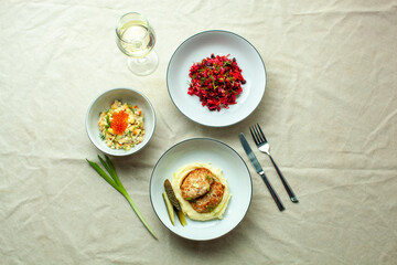 Elegant three course business lunch on beige tablecloth with beetroot salad, herring, potato cutlet, mashed potatoes, pickles, and white wine. Perfect for a fancy restaurant meal